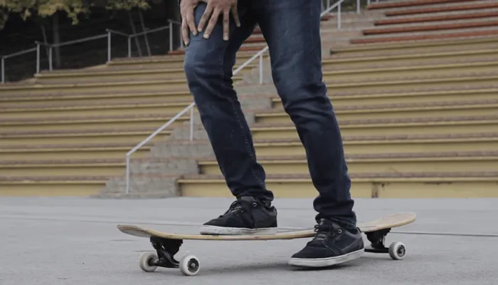 A rider standing on a longboard with one foot over the deck edge on a paved square