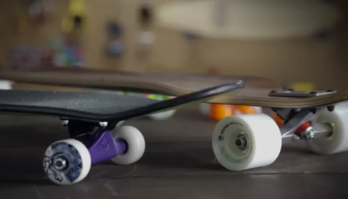 Two longboards seen at wheel level, one with purple trucks and one with white wheels
